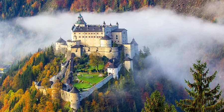 The picturesque castle of Burg Hohenwerfen is surrounded by colourful autumnal trees and a blanket of mist. 
